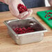 A person in gloves holding a Vollrath stainless steel steam table pan filled with pomegranate seeds.