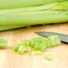 Fresh celery cut into pieces on a cutting board next to a knife.