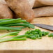 A cutting board with a knife and green onions next to a potato.