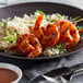 A plate of grilled shrimp skewers coated in a spicy sauce, served over white rice with sliced green onions.