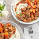 A bowl of beef stew with meat, carrots, and potatoes.