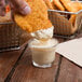 A person dipping a piece of fried chicken into a small glass of Ken's Honey Mustard Dressing.