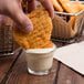 A hand dipping a potato chip into a small glass of Ken's honey mustard dressing.