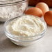 A close-up of a bowl of white powder next to a group of eggs.