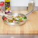 A person stirring yellow and pink onions and vegetables in a Vollrath stainless steel fry pan.