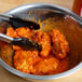 A bowl of Texas Pete buffalo wings with tongs.