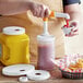 A person using a Tablecraft Maxi Pelican Pump to pour ketchup into a yellow plastic container.