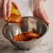 A person pouring Sweet Baby Ray's Golden BBQ & Wing sauce into a bowl of food.