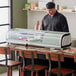 A man standing behind a countertop with food in a refrigerated display.