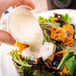 A person pouring Ken's Foods Deluxe Bleu Cheese Dressing on a salad with vegetables.