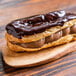 A chocolate covered eclair on a wooden surface.