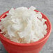 A red bowl filled with white medium chipped coconut.