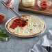 A person using a spatula to spread red sauce on a Venice Bakery gluten-free vegan pizza crust.