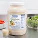 A jar of Ken's Foods Creamy Caesar Dressing next to a bowl of salad.