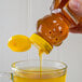 A hand pouring Natural American Honey from a bear-shaped bottle into a glass of liquid.