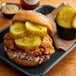 A chicken sandwich with Nathan's Famous Sweet Horseradish Pickle slices on a plate.