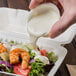 A hand pouring Ken's Bleu Cheese dressing over a salad.