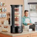 A man standing behind an Avantco Black Countertop Rotating Refrigerated Cake Display filled with cakes.