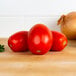 A close up of plum tomatoes and an onion on a table.