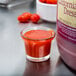 A small glass cup with red liquid next to a container of Ken's California French Dressing and tomatoes.