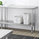 A Regency stainless steel work table undershelf with metal containers on it.