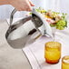 A hand pouring water into a stainless steel Acopa bell pitcher with ice guard.