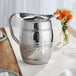 An Acopa stainless steel bell pitcher on a table with flowers.