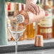 A bartender using an Acopa copper cobbler cocktail shaker to pour a drink into a martini glass.