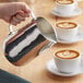 A person pouring milk into a cup of coffee using a Choice polished stainless steel frothing pitcher.