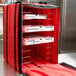 A red nylon American Metalcraft delivery bag with shelves inside holding pizza boxes.