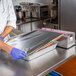 A man using the Choice stainless steel film and foil dispenser and cutter to cut foil on a metal table.