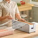 A stainless steel film and foil dispenser and cutter being used to cover a food container with plastic wrap.