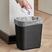 A hand throwing crumpled paper into a black rectangular Continental trash can.