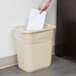 A hand putting a piece of paper into a beige rectangular trash can.