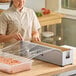 A stainless steel film and foil dispenser and cutter being used to cover a food container with plastic wrap.