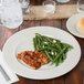 An ivory china plate with green beans and chicken on it.