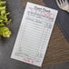 A white and green Adams guest check receipt with writing next to a fork and knife on a table.