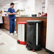 A man in blue scrubs using a black Rubbermaid linen hamper.