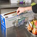 A hand using a Choice Safety Slide Cutter to put plastic wrap on a box of fruit.