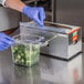 A person in blue gloves using a Choice stainless steel film and foil cutter to cover a container with plastic film.