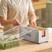 A stainless steel film and foil dispenser and cutter being used to cover a container of greens with plastic wrap.