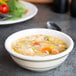 A Tuxton eggshell china bowl with green bands filled with soup with vegetables and rice.