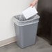 A hand putting a piece of paper into a gray Continental rectangular trash can.