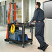 A man pushing a Rubbermaid utility cart with tools.