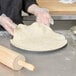 A person in gloves using a rolling pin to make pizza dough on an American Metalcraft perforated pizza pan.