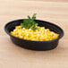 A Pactiv Newspring VERSAtainer oval microwavable container filled with corn and parsley.