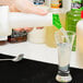 A hand pouring liquid from a green and white Carlisle plastic container into a glass.