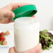 A hand pouring white liquid into a Carlisle white jar with a green lid.