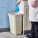 A man in a lab coat putting a blue glove in a Rubbermaid medical wastebasket.