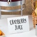 A white table with a juice dispenser and a sign with black text.